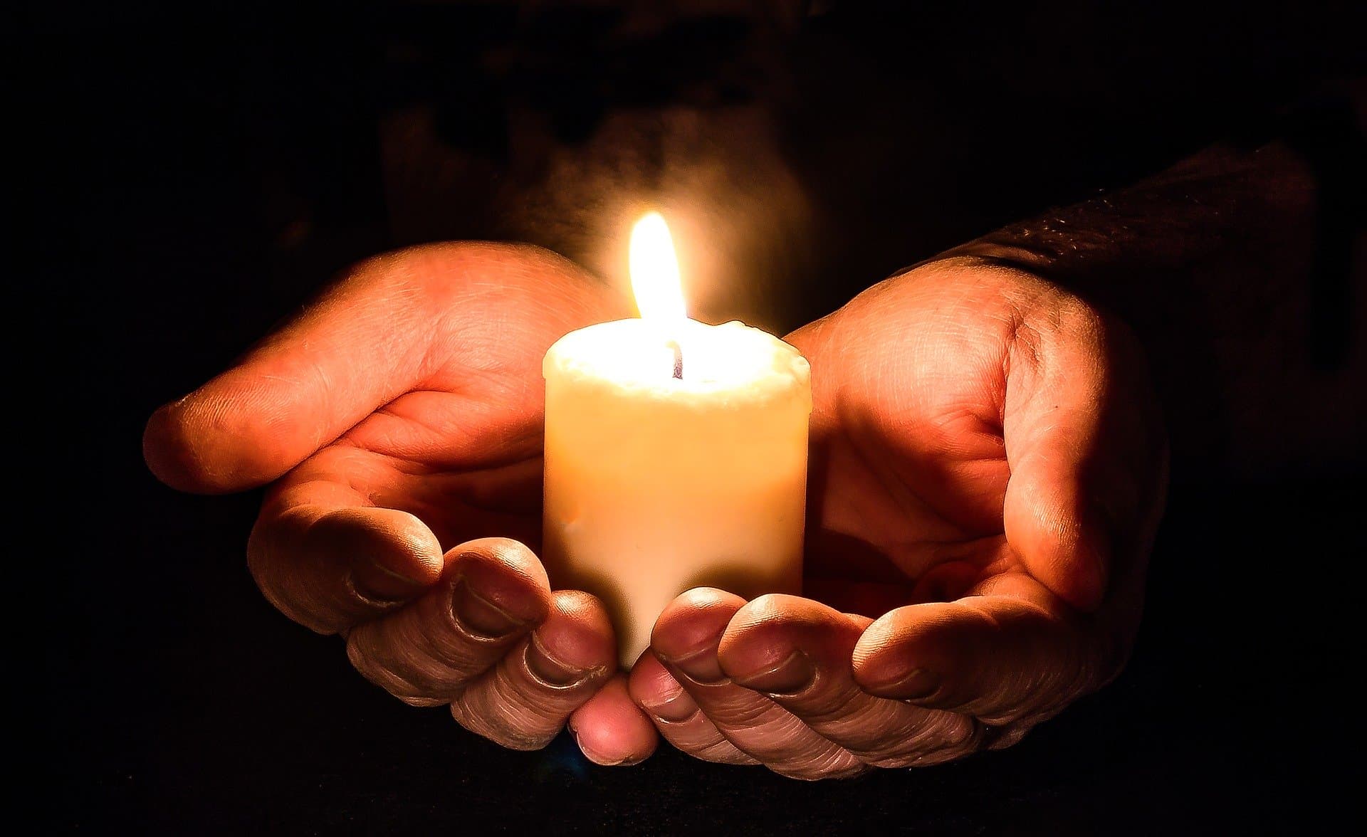 Hands cradling a lit candle in the dark